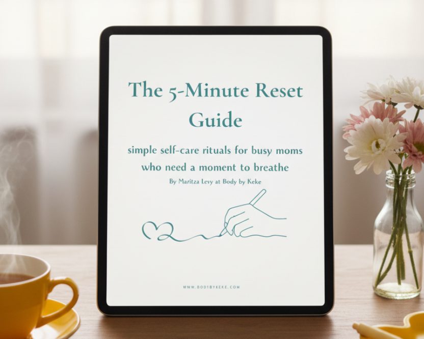 A white booklet or guide titled "The 5-Minute Reset Guide" lies on a light neutral surface, styled with a yellow cup on the left and a yellow heart-shaped dish on the right. The cover has teal text and a simple line drawing of a hand writing a heart.