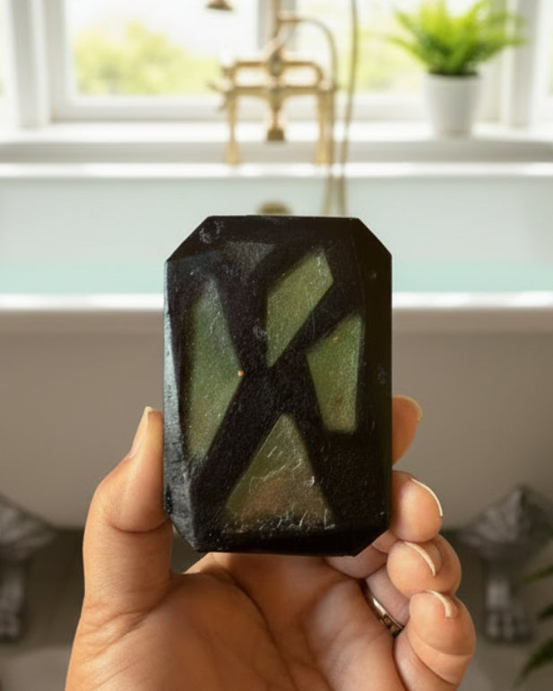 Hand holding black and green soap bar with bathtub in background