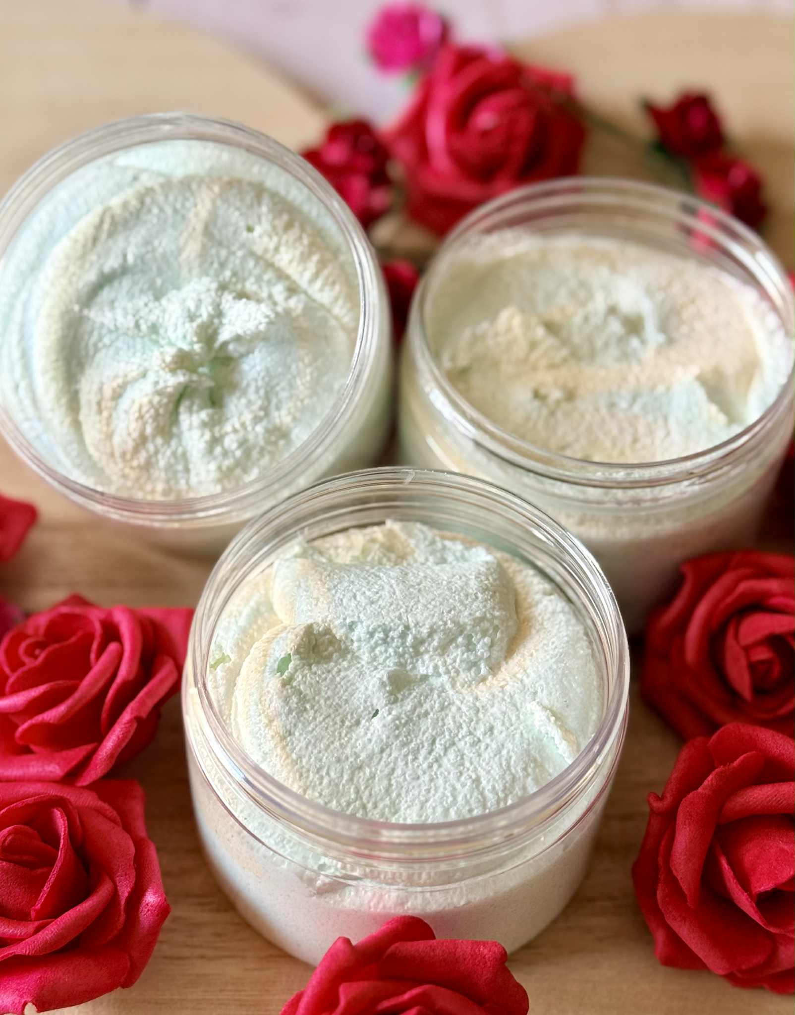 Three jars of white and green sugar scrub with red roses around them on a wooden surface
