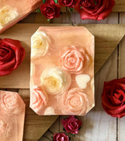 Bar of soap with rose and heart designs surrounded by red and pink roses on a wooden surface