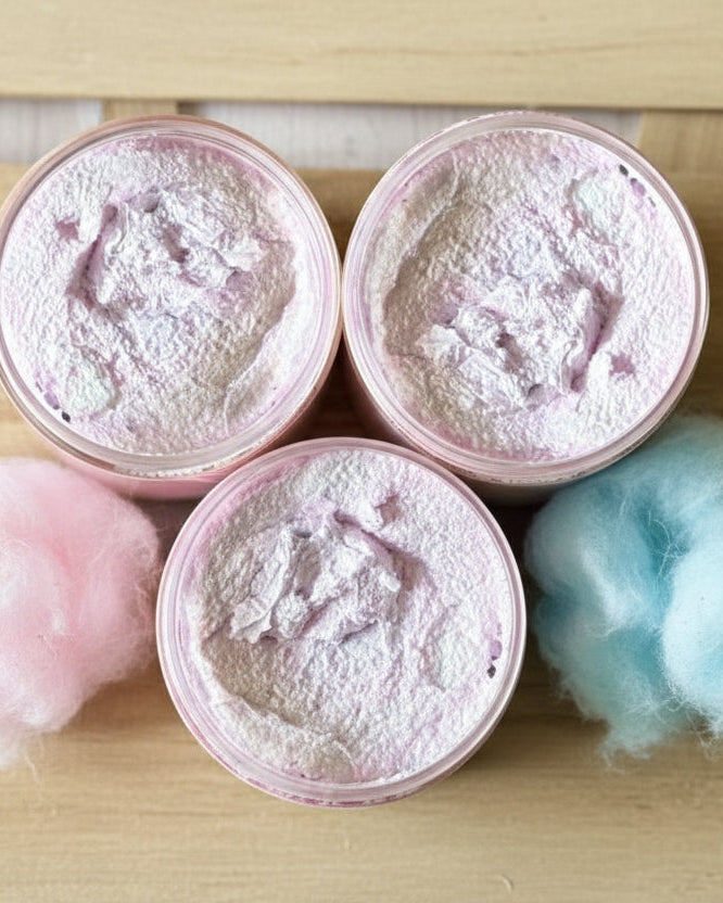 Three containers of a pink sugar scrub on a wooden surface with pink and blue cotton candy