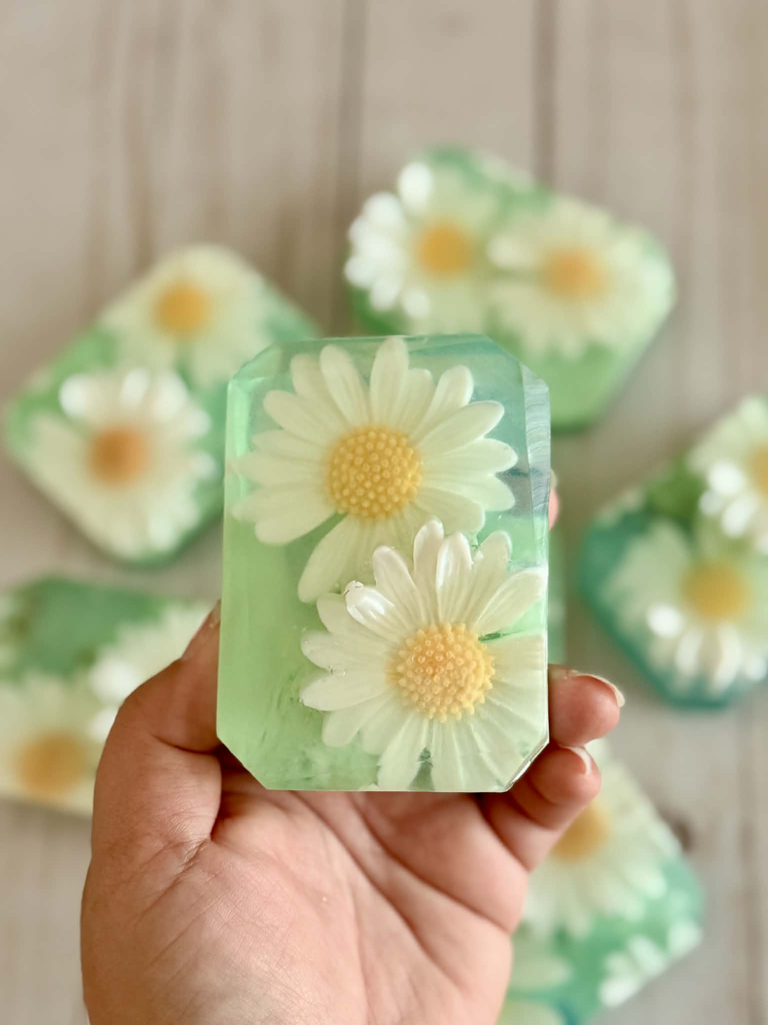 Hand holding a green soap bar with daisy flowers against a neutral background