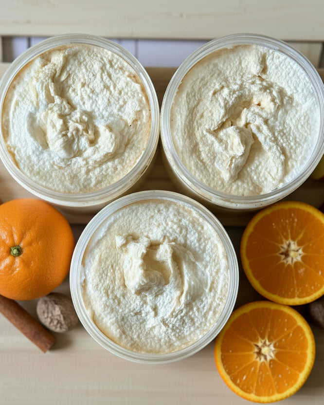 Three containers of a white sugar scrub on a wooden board with fruits and spices.