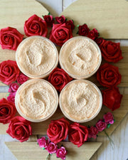 Four containers of a beige product surrounded by red and pink roses on a wooden heart-shaped board.