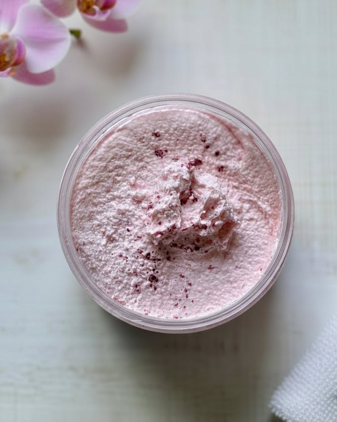 Jar of pink creamy sugar scrub with flower in background