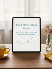 A white booklet or guide titled "The 5-Minute Reset Guide" lies on a light neutral surface, styled with a yellow cup on the left and a yellow heart-shaped dish on the right. The cover has teal text and a simple line drawing of a hand writing a heart.