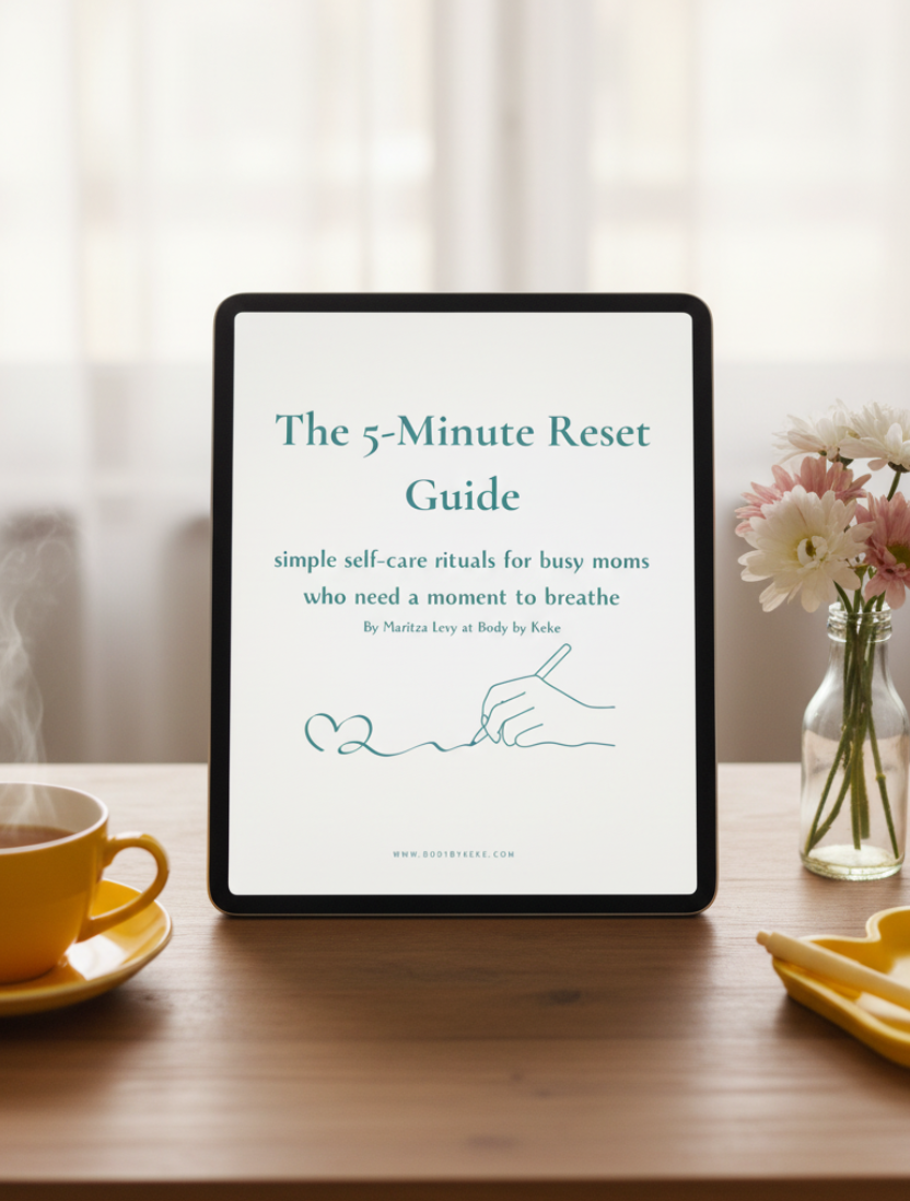 A white booklet or guide titled "The 5-Minute Reset Guide" lies on a light neutral surface, styled with a yellow cup on the left and a yellow heart-shaped dish on the right. The cover has teal text and a simple line drawing of a hand writing a heart.