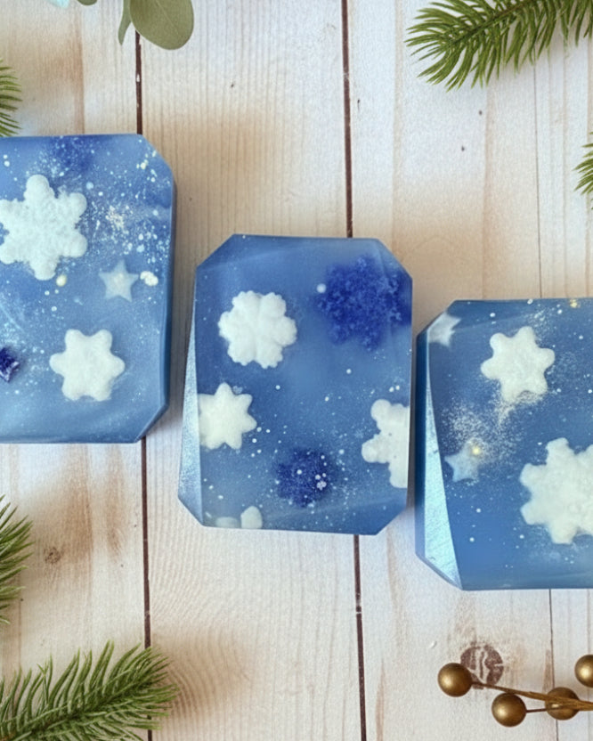 Blue soaps with snowflake designs on a wooden surface with fir