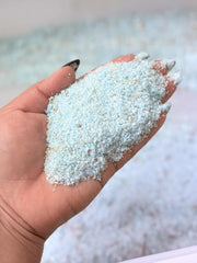 Hand holding a small amount of light blue sand with a blurred background